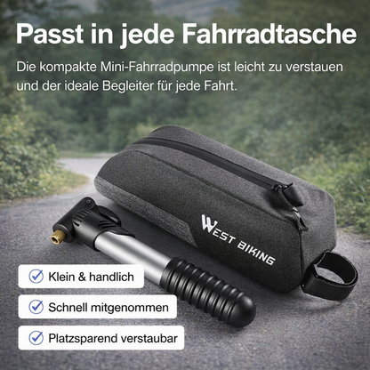 Mini-Fahrradpumpe neben einer Fahrradtasche auf Asphalt, kompakt und transportbereit dargestellt.